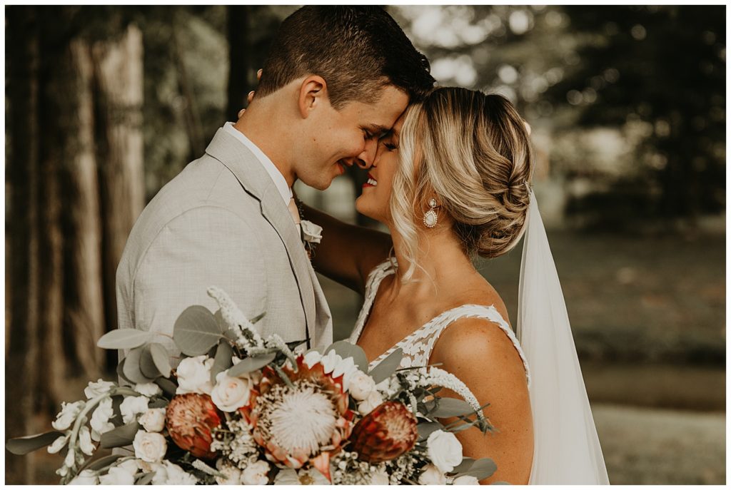 bride in boho lace wedding dress and blush bouquet with king protea and eucalyptus, groom in light grey suit