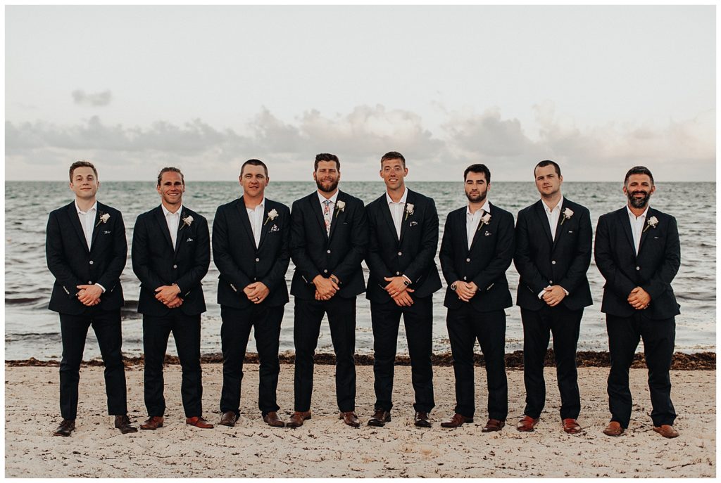 groom and groomsmen taking photos on the beach before wedding ceremony in cancun mexico