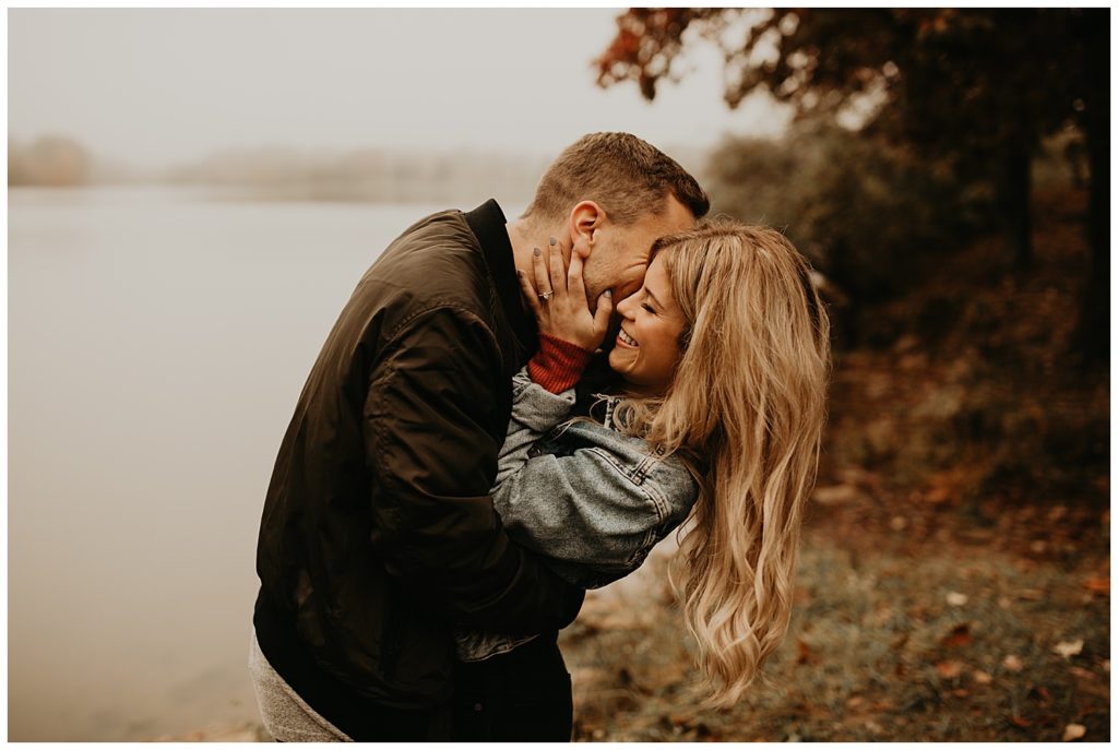 Engaged couple taking portraits by the river in Kentucky, surrounded by fall leaves