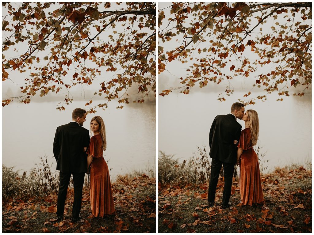 Engaged couple taking portraits by the river in Kentucky, surrounded by fall leaves. Girl is wearing a rust colored velvet dress