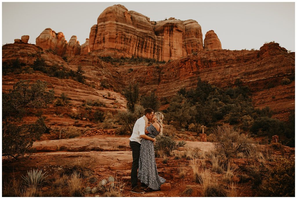 engaged couple kissing in front of red rock in sedona