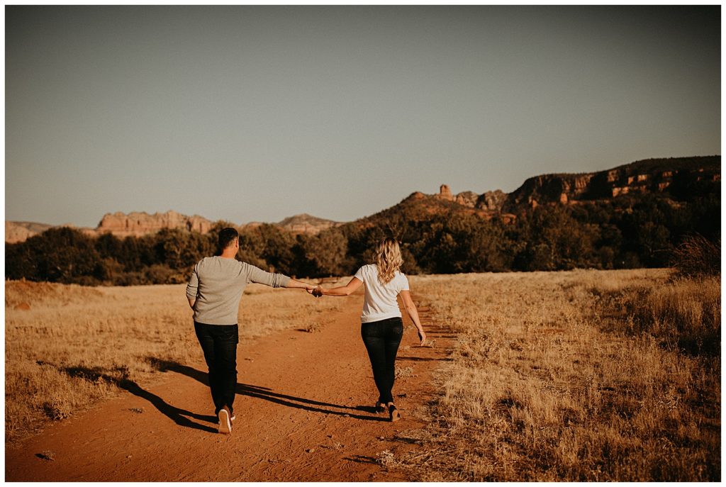 couple holding hands while taking engagement photos at cathedral rock