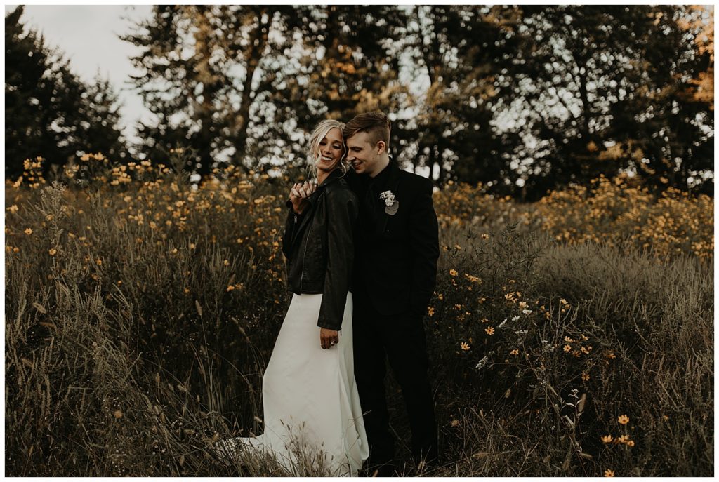 groom wearing black suit and boutonniere bride wearing black leather jacket and wedding dress